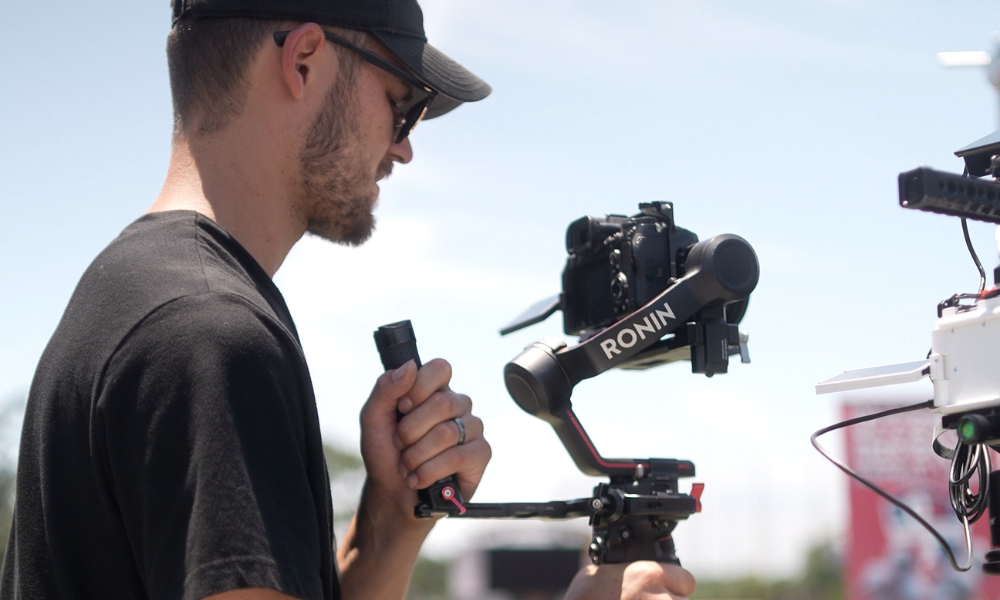 RBV Media A person wearing a black shirt and cap operates a camera mounted on a Ronin gimbal stabilizer outdoors in daylight. Myrtle Beach, Content, Ads, Web, Social, Email