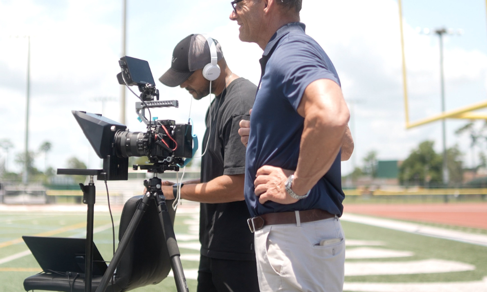 RBV Media Two men stand on a football field next to a professional video camera setup; one operates the equipment while the other observes. Myrtle Beach, Content, Ads, Web, Social, Email